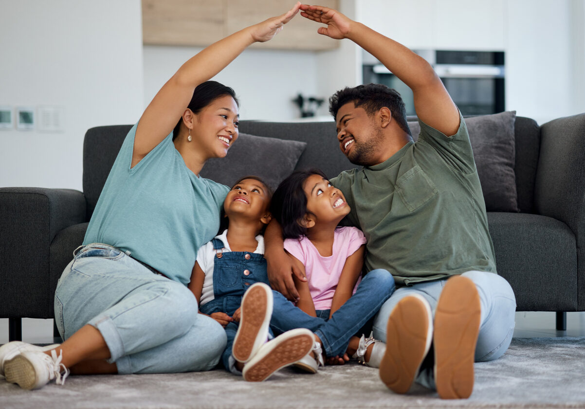 Happy family, floor and hands roof for safety, support and care or affection in home. Love, protection or house insurance symbol, caring parents and kids or girls sitting bonding in security together